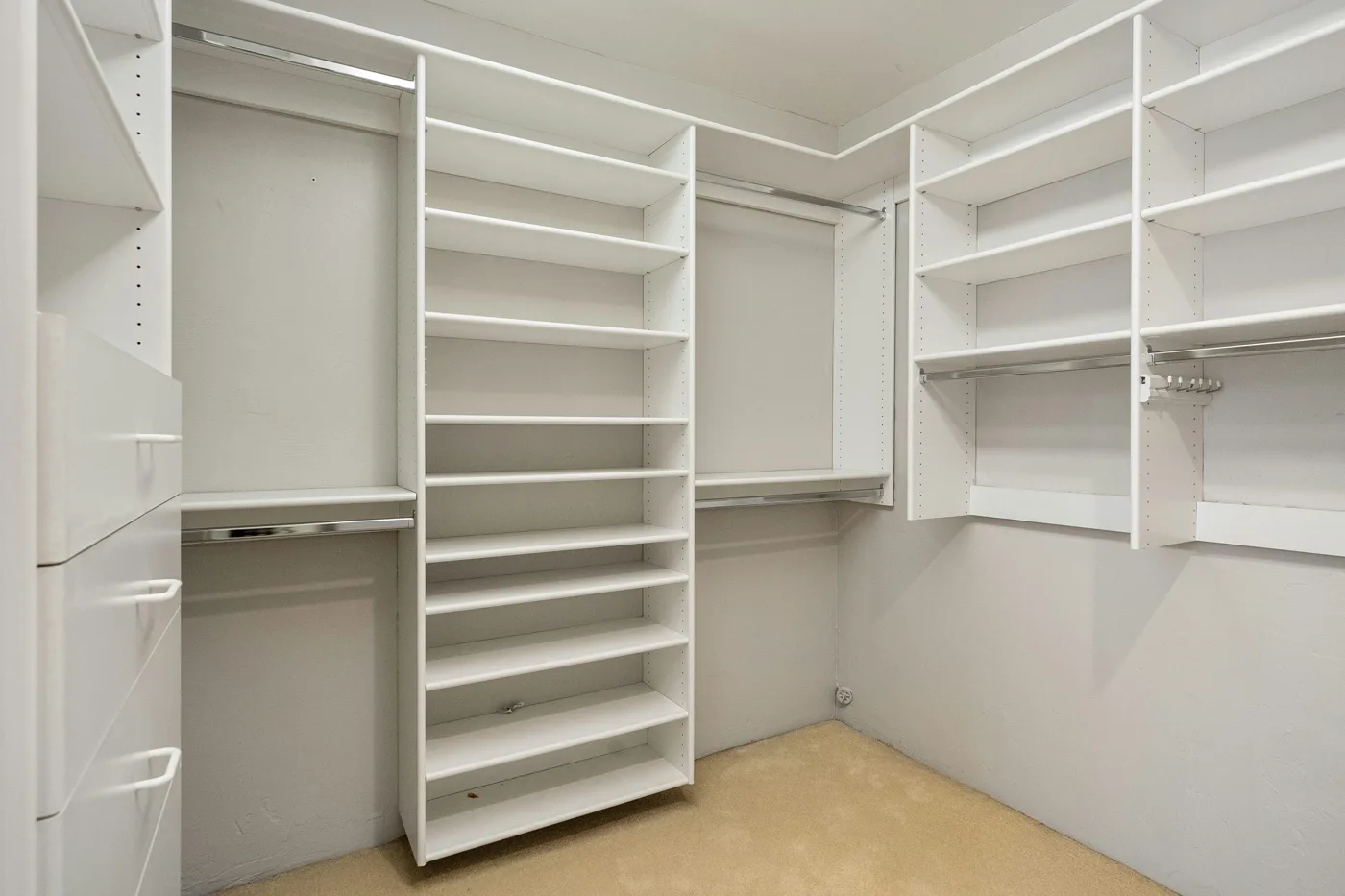 Empty walk-in closet with white adjustable shelves, hanging rods, and a drawer bank.