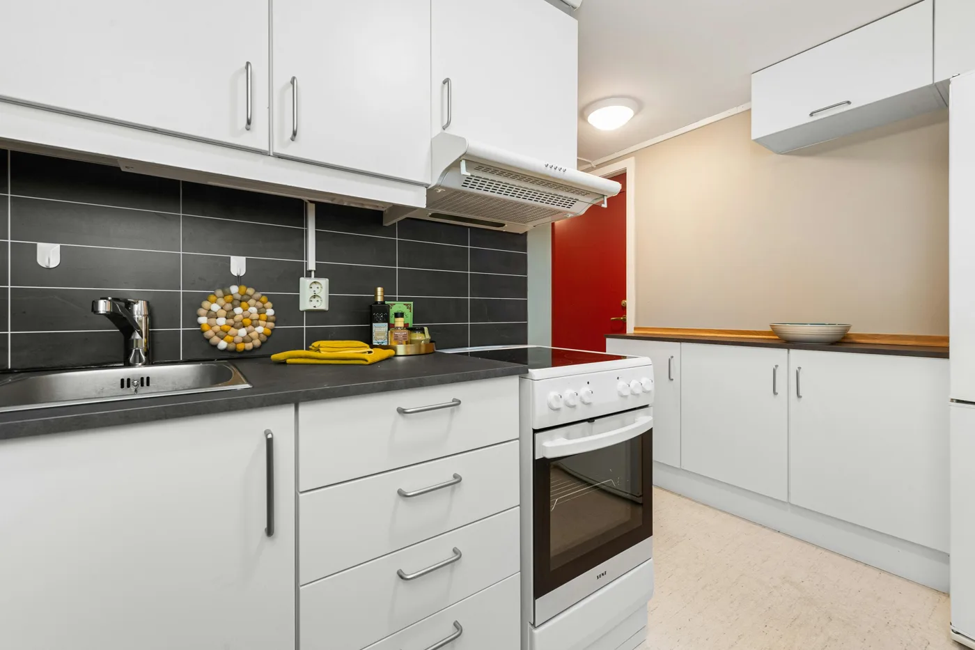 Compact kitchen with white cabinets, dark countertops, and a dark rectangular-tile backsplash.