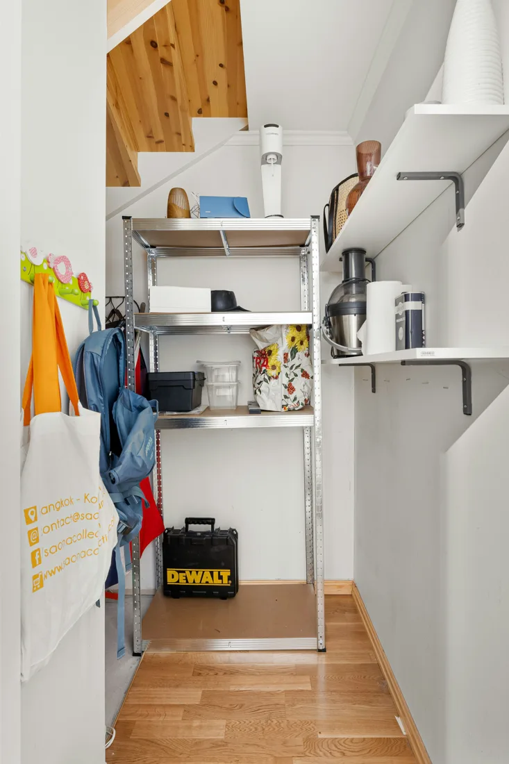 Compact storage space under stairs with bracket-supported white shelves and a freestanding metal rack.