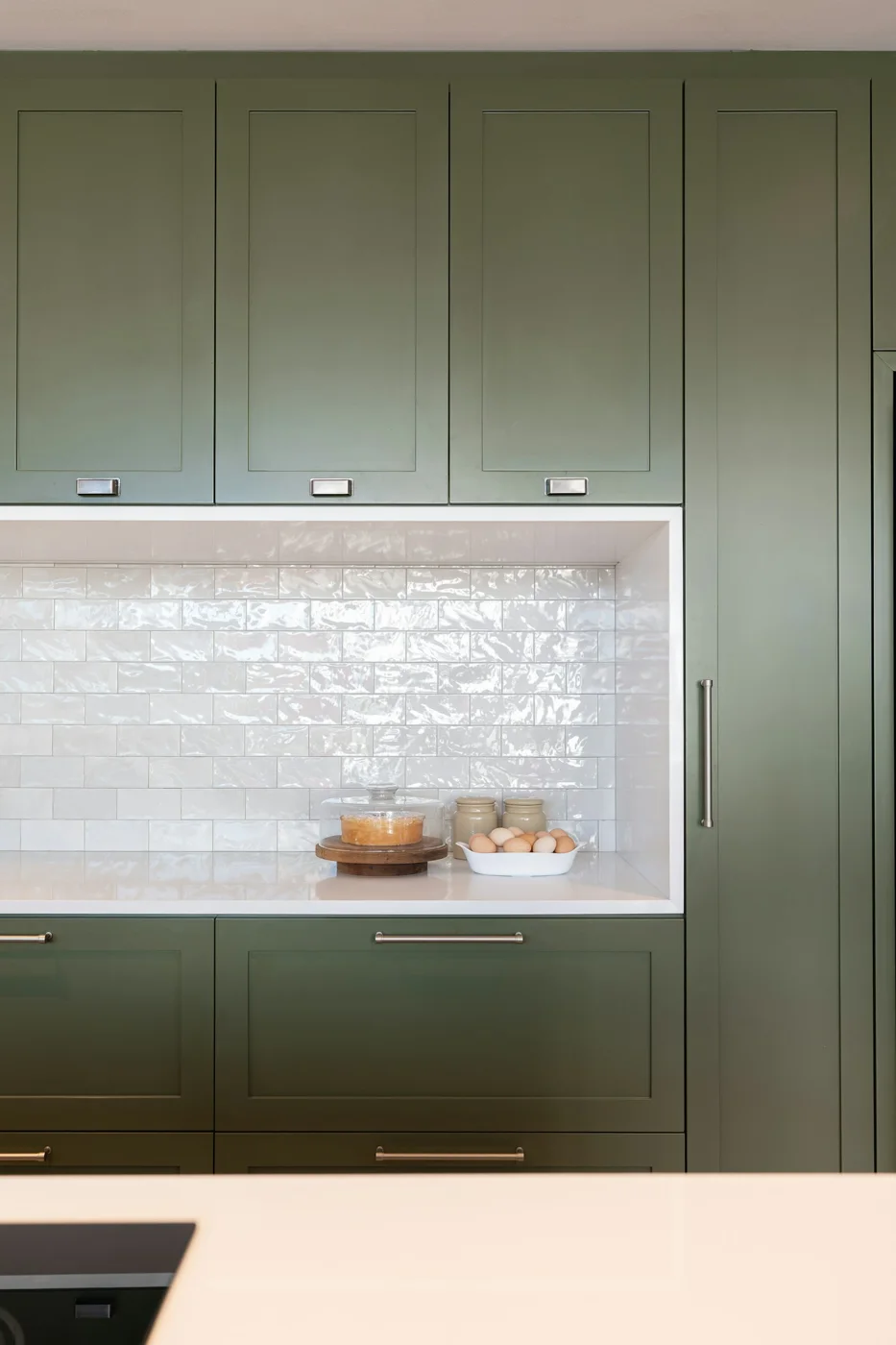 Green kitchen cabinets with white subway tile backsplash and countertop