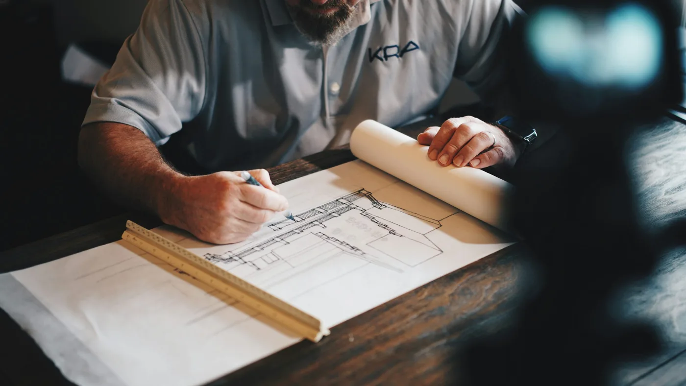 Person using a pencil and ruler to review an architectural drawing at a desk